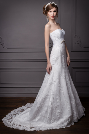 beautiful sweet gentle girl groom in a wedding dress with a wreath and flowers in her hair in the studioの写真素材
