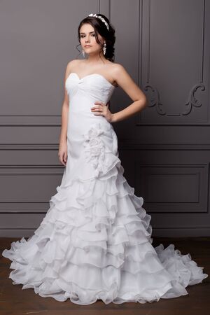 beautiful sweet gentle girl groom in a wedding dress with a wreath and flowers in her hair in the studioの写真素材