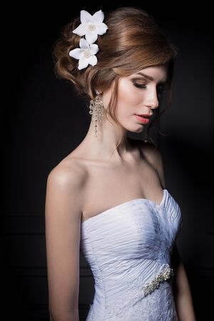 beautiful sweet gentle girl groom in a wedding dress with a wreath and flowers in her hair in the studioの写真素材