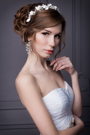 beautiful sweet gentle girl groom in a wedding dress with a wreath and flowers in her hair in the studioの写真素材