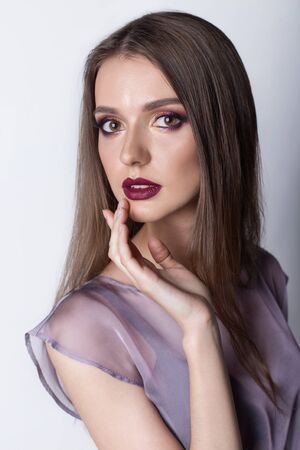Portrait of a beautiful girl with a sweet delicate burgundy lips and bright makeup in a light transparent negligee studio on a white backgroundの写真素材