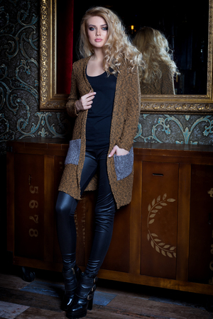 Beautiful young sexy woman with long blond hair, bright make-up Smokey Eyes wearing a sweater next to a dresser and a bar with a catalog of clothing collection autumn fashion spring styleの写真素材