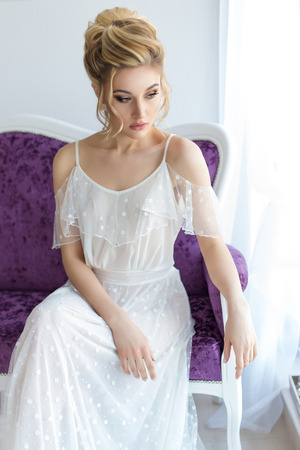 beautiful cute sweet young girl in a light dress beautiful boudoir with bright makeup smokey eyes with a beautiful evening hairstyle and jewelry handmadeの写真素材
