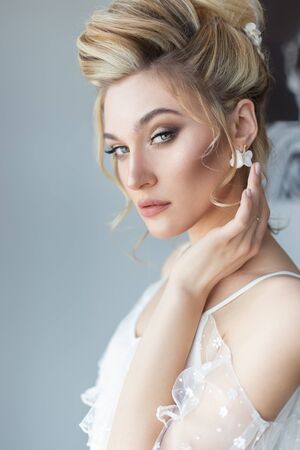 beautiful cute sweet young girl in a light dress beautiful boudoir with bright makeup smokey eyes with a beautiful evening hairstyle and jewelry handmadeの写真素材