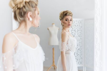 beautiful cute sweet young girl in a light dress beautiful boudoir with bright makeup smokey eyes with a beautiful evening hairstyle and jewelry handmadeの写真素材
