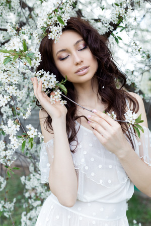 beautiful cute sweet sexy girl bride with a gentle eye make-up full lips in white light dress walks in the lush garden on a warm spring dayの写真素材
