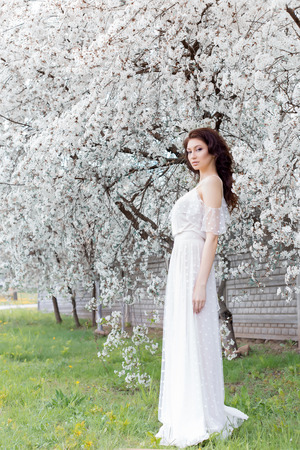 beautiful cute sweet sexy girl bride with a gentle eye make-up full lips in white light dress walks in the lush garden on a warm spring dayの写真素材