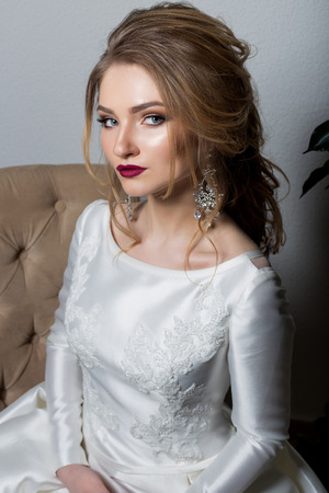 portrait of a beautiful sexy cute girl happy bride in an elegant dress with bright makeup in a white dress with a gorgeous wedding hairstyleの写真素材