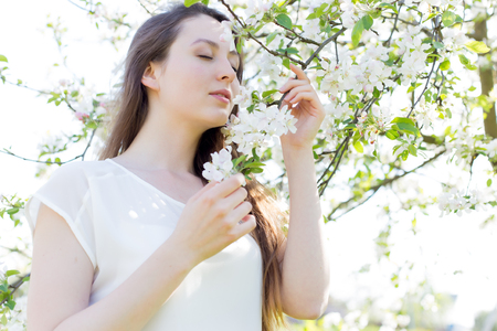 beautiful sweet girl in a white shirt with blooming apple trees in the garden walks bright warm summer dayの写真素材