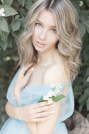 beautiful sexy tender blonde girl in a blue light dress with a sprig of jasmine in his hands sitting in the garden in the style of photos Fine Artの写真素材