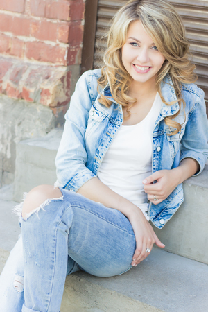 beautiful funny blonde girl with big lips with a charming smile, wearing jeans and a white shirt walking in the city solnetsnym summer dayの写真素材