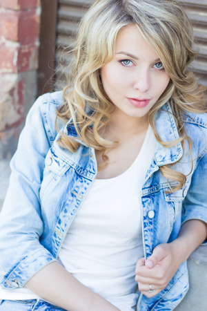beautiful funny blonde girl with big lips with a charming smile, wearing jeans and a white shirt walking in the city solnetsnym summer dayの写真素材
