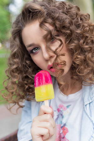 beautiful girl with curly with a naked sexy lips eating color ice cream in a cafe in the park a bright summer dayの写真素材