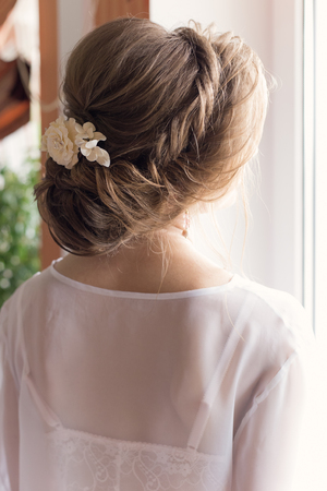 morning beautiful happy young girl of the bride near a window in a white dress with a beautiful boudoir evening festive hairdo with ornaments in their hair and soft makeupの写真素材