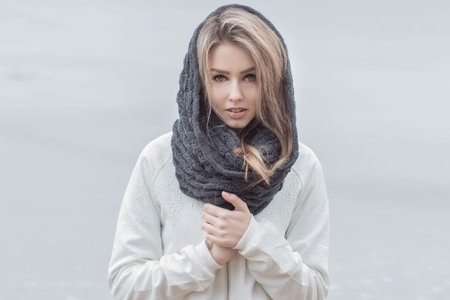 beautiful girl with beautiful lips in a white jacket with a warm scarf on the head in cold weatherの写真素材