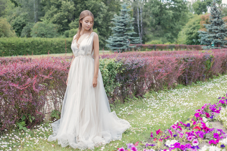 Beautiful tender young woman bride in her wedding dress gentle air walks in the lush garden on a hot sunny summer dayの写真素材