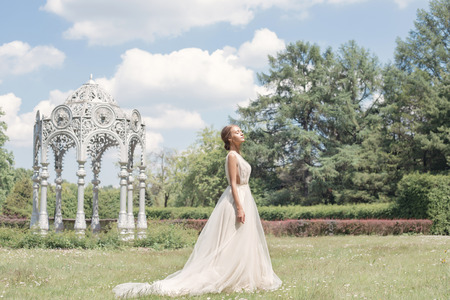 Beautiful tender young woman bride in her wedding dress gentle air walks in the lush garden on a hot sunny summer dayの写真素材