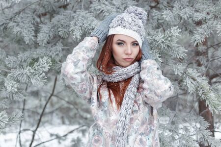 beautiful cheerful cute red-haired girl in a cap and scarf plays with snow in the beautiful forest fairyの写真素材