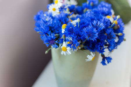 beautiful big bouquet of wild flowers of cornflowers and daisies standing on a table in a potの写真素材