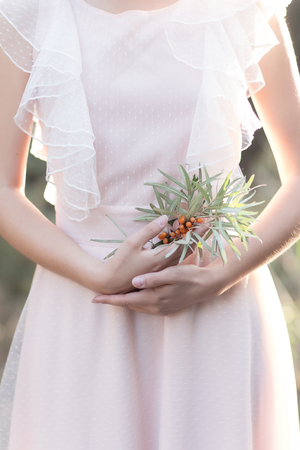 gentle graceful hands of a bride Girl with a branch of sea buckthorn in the hand in a gentle air wedding dress in the sun rays at sunsetの写真素材