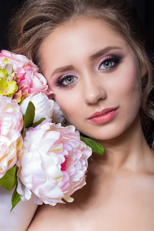portrait of a beautiful cute sweet girl with a beautiful bride with bright makeup evening wedding hairstyle with a bouquet of flowers in the studio on a black backgroundの写真素材
