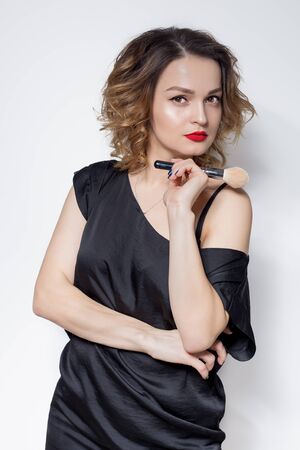beautiful sexy girl makeup with red lipstick standing with cosmetic brush in his hand in the studio on a white backgroundの写真素材