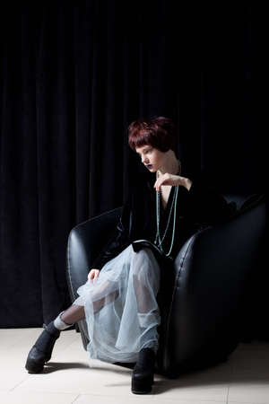 fashion shot of a beautiful young girl with a cheeky short hair style hipster in black velvet jacket in a studio on a black backgroundの写真素材