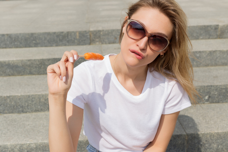 Beautiful young sexy girl in sunglasses eating ice cream on the ladder and licking plump lips a bright sunny hot dayの写真素材