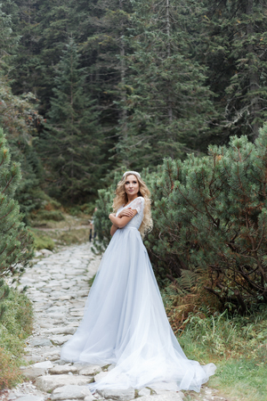 beautiful gentle girl bride in the air fairy blue wedding dress with luxurious curls in the mountains near the lake with a crown utterlyの写真素材