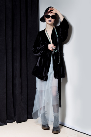 fashion shot of a beautiful young girl with a cheeky short hair in a hipster style in a black velvet jacket in Kupka Chesney and sunglasses in a studio on a black backgroundの写真素材