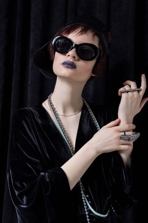 fashion shot of a beautiful young girl with a cheeky short hair in a hipster style in a black velvet jacket in Kupka Chesney and sunglasses in a studio on a black backgroundの写真素材