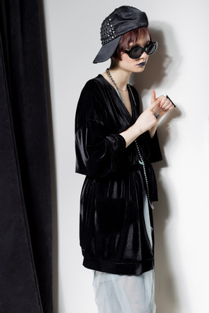 fashion shot of a beautiful young girl with a cheeky short hair in a hipster style in a black velvet jacket in Kupka Chesney and sunglasses in a studio on a black backgroundの写真素材