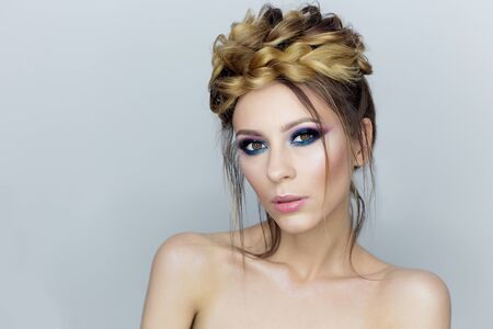 Fashionable portrait of a beautiful sexy girl with crazy hairstyle with bright colored makeup with bared shoulders in the studio on a white backgroundの写真素材