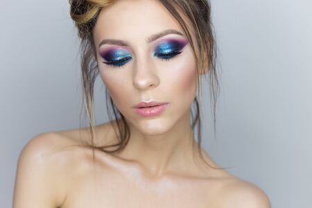 Fashionable portrait of a beautiful sexy girl with crazy hairstyle with bright colored makeup with bared shoulders in the studio on a white backgroundの写真素材
