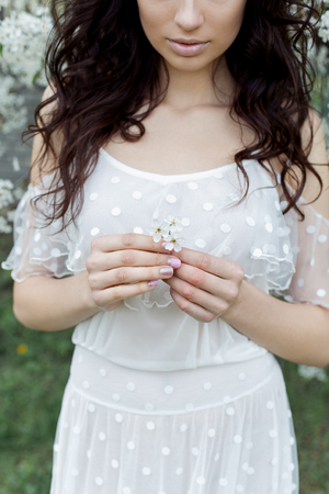 Beautiful sexy girl with a gentle make-up in a long light dress among the flowering trees walks in the spring garden on a warm sunny dayの写真素材