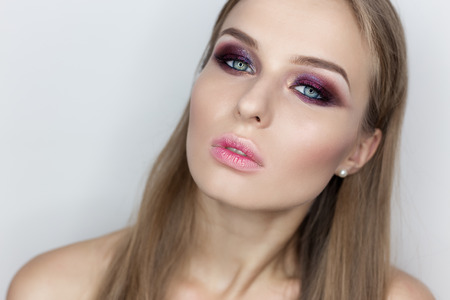 Fashionable portrait of a beautiful sexy girl with crazy hairstyle with bright colored makeup with bared shoulders in the studio on a white backgroundの写真素材