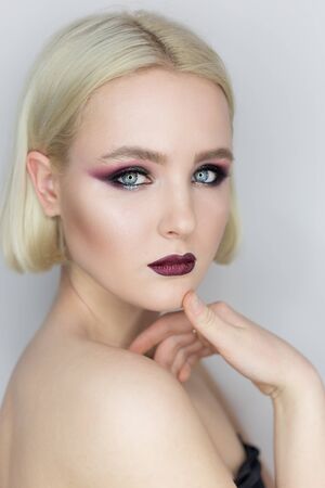 Fashionable portrait of a beautiful sexy girl with crazy hairstyle with bright colored makeup with bared shoulders in the studio on a white backgroundの写真素材