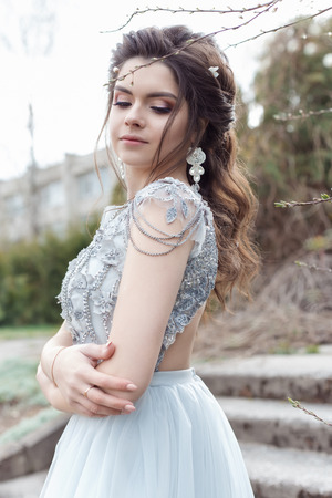 Beautiful young tender gay girl with a beautiful wedding hairstyle with a snow-white smile in a light dress is walking in a spring blooming gardenの写真素材