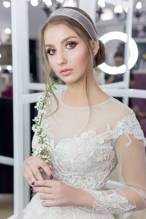 Beautiful cute tender young girl bride in wedding dress in mirrors with evening hair and gentle light make-upの写真素材