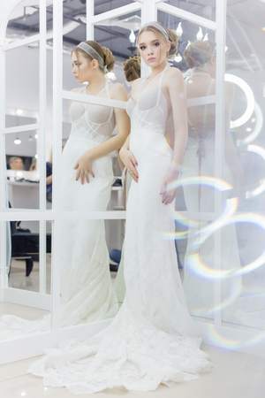 Beautiful cute tender young girl bride in wedding dress in mirrors with evening hair and gentle light make-upの写真素材