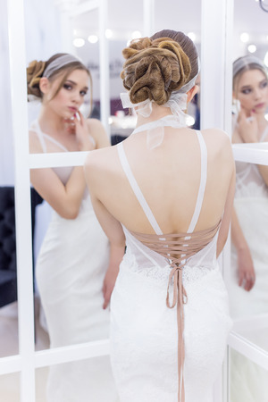 Beautiful cute tender young girl bride in wedding dress in mirrors with evening hair and gentle light make-upの写真素材