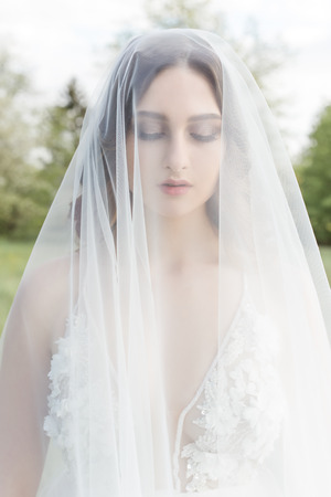 Beautiful sweet girl bride in a gentle air wedding dresses veil in a blooming spring garden in the rays of the sunlight at sunset. Fine art styleの写真素材