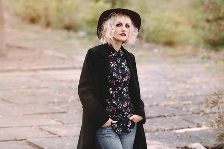 Beautiful cheerful blonde girl with short curly hair in coat and hat walking outdoors on stairsの写真素材