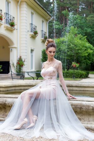 Beautiful elegant girl in evening dress with beautiful evening festive hairdo near fountainの写真素材