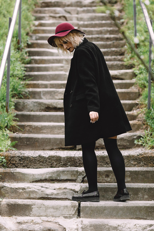 Beautiful cute girl in red hat and black coat walking in the cityの写真素材