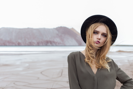 Beautiful, sexy blond girl posing in the mountains on a cracked ground in a black hat with bright make-upの写真素材