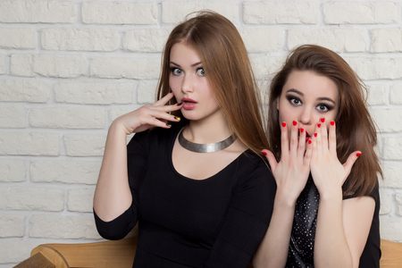 two beautiful young girls in black dresses sit on the bench and gossipの写真素材