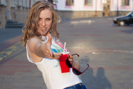 beautiful cute girl with curly hair in sunglasses with a paper glass and a straw drinking a drink in the city on a sunny summer eveningの写真素材