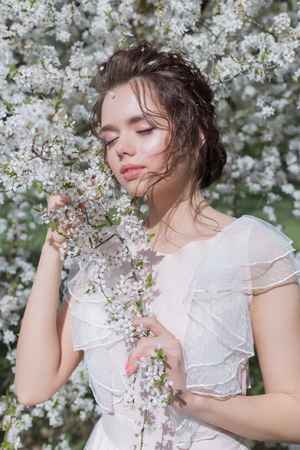 beautiful tender sweet girl in a pink dress with a hairdo near blossoming tree on a sunny spring dayの写真素材