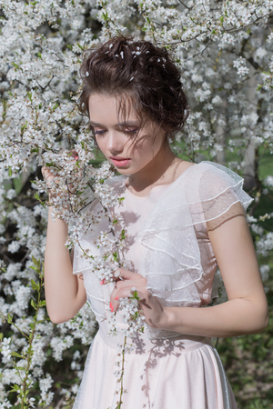 beautiful tender sweet girl in a pink dress with a hairdo near blossoming tree on a sunny spring dayの写真素材